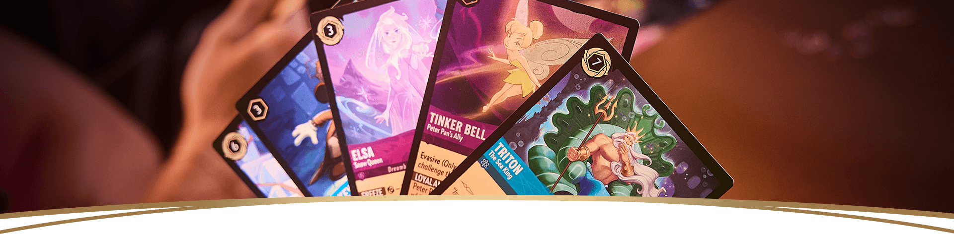 Several Disney Lorcana cards fanned out, showing Elsa, Tinker Bell, and Triton
